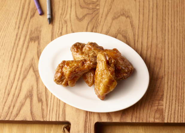 Jumbo Sauced Chicken Wings on a Round White Plate, Close Up on a Wooden Cutting Board with Crayons for Kids