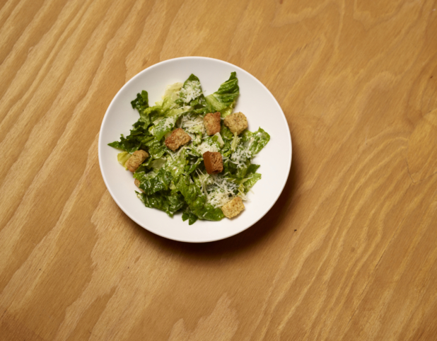 Overhead View of a Classic Caesar Salad with Croutons on a Round White Plate on a Rustic Wooden Surface