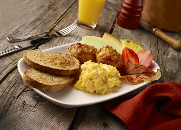 Breakfast Platter of Scrambled Eggs, Bacon, Fresh Fruit, Potato Latkes and Toasted Rye Bread on a Rectangular White Ceramic Platter on a Rustic Wood Surface
