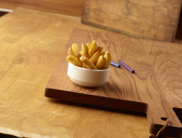 Small Kids Size Thick Cut French Fries in a Round White Bowl on a Wooden Cutting Board on a Wood Surface with Crayons for Kids