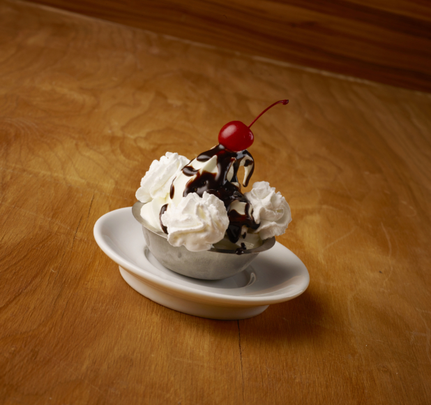 Vanilla Ice Cream Sundae with Chocolate Sauce, Maraschino Cherry and Whipped Cream in a Stainless Steel Bowl on a Wooden Table