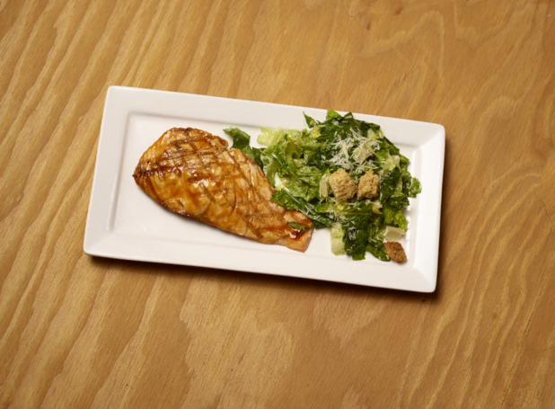 Overhead View of Grilled Salmon Teriyaki with a Side of Caesar Salad on a White Rectangular Platter Dish on a Wooden Surface