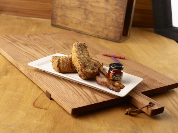 French Toast, Bacon Strips and a Mini Jar of Maple Syrup on a Rectangular White Platter Dish on a Wooden Cutting Board with Crayons for Kids