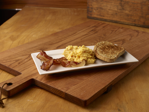Sliced Toasted Rye Bread with Scrambled Bread and Bacon Strips on a Rectangular White Platter Dish on a Wooden Cutting Board