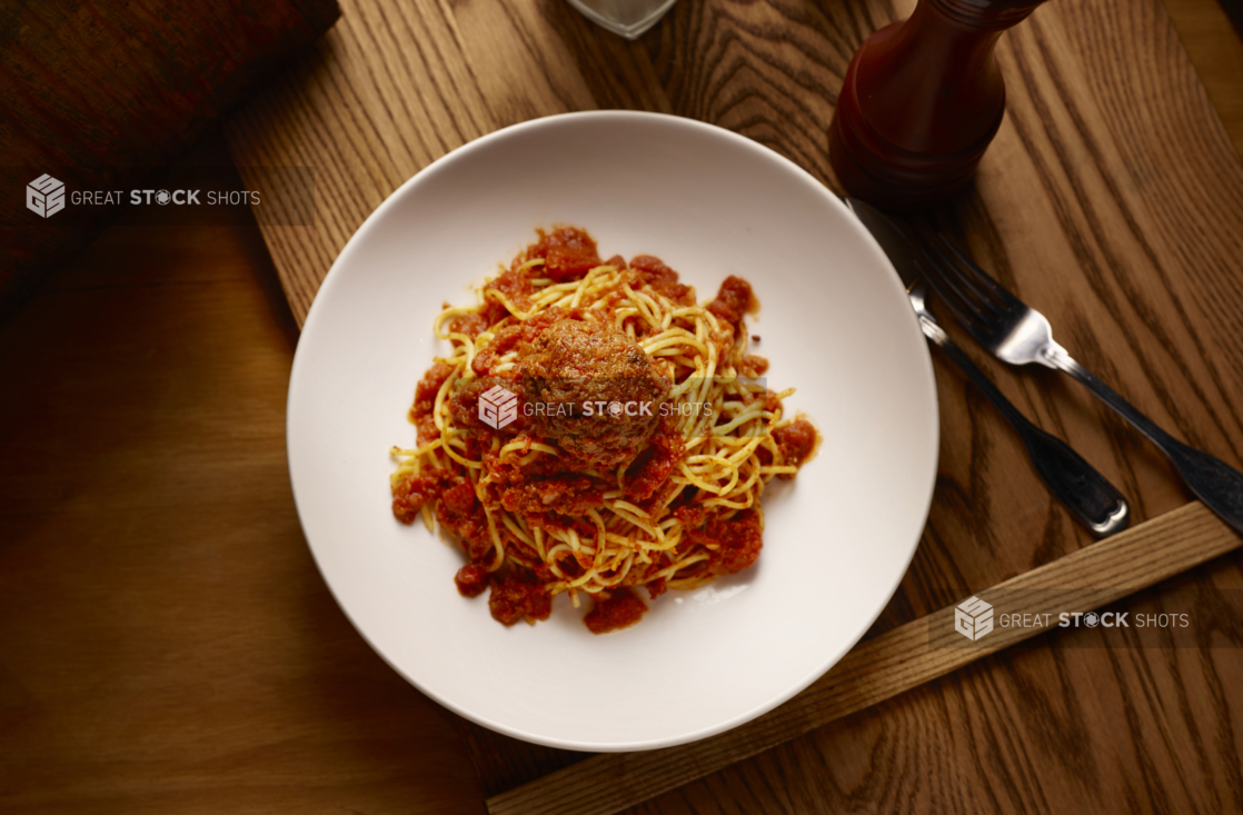 Overhead View of a Kids Spaghetti and Meatball in a Large White Ceramic Bowl on a Wooden Cutting Board in an Indoor Setting