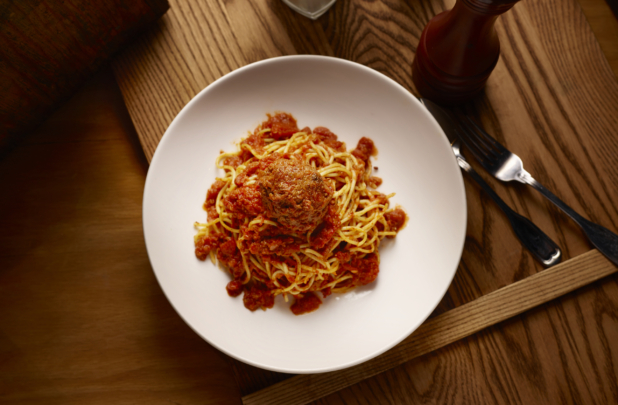 Overhead View of a Kids Spaghetti and Meatball in a Large White Ceramic Bowl on a Wooden Cutting Board in an Indoor Setting