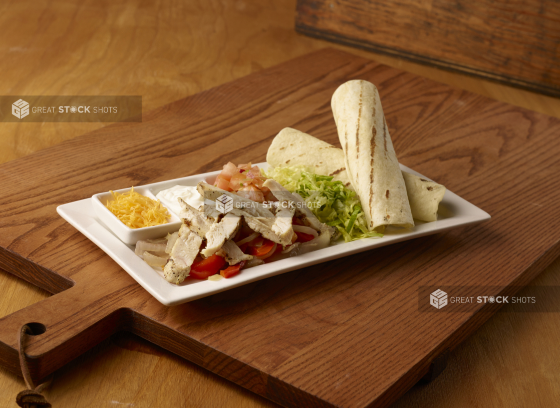 Kids Grilled Chicken Fajita Platter on a Rectangular White Ceramic Dish with Fresh and Cooked Ingredients and Toppings on a Wooden Cutting Board in an Indoor Setting