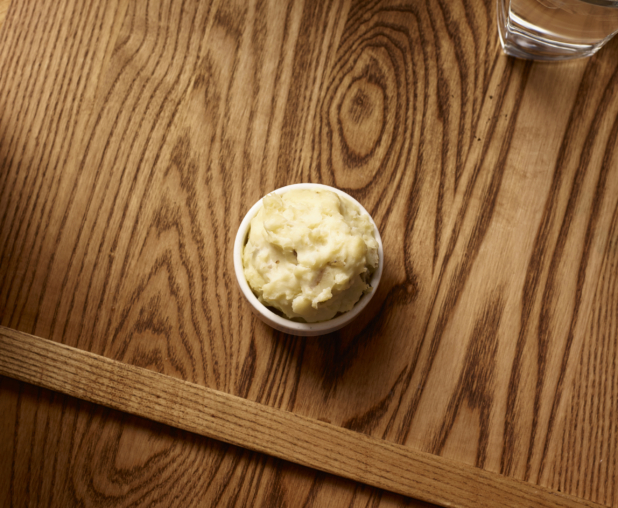 Overhead View of a Small White Ceramic Dish of Kid-Sized Mashed Potatoes Side Dish on a Wooden Cutting Board in an Indoor Setting