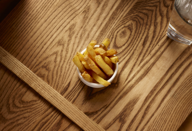 Overhead View of a Small Kids Size Thick Cut French Fries in a Round White Bowl on a Wooden Cutting Board in an Indoor Setting