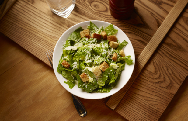 Overhead View of a Caesar Salad in a Round White Ceramic Dish on a Wooden Cutting Board in an Indoor Setting