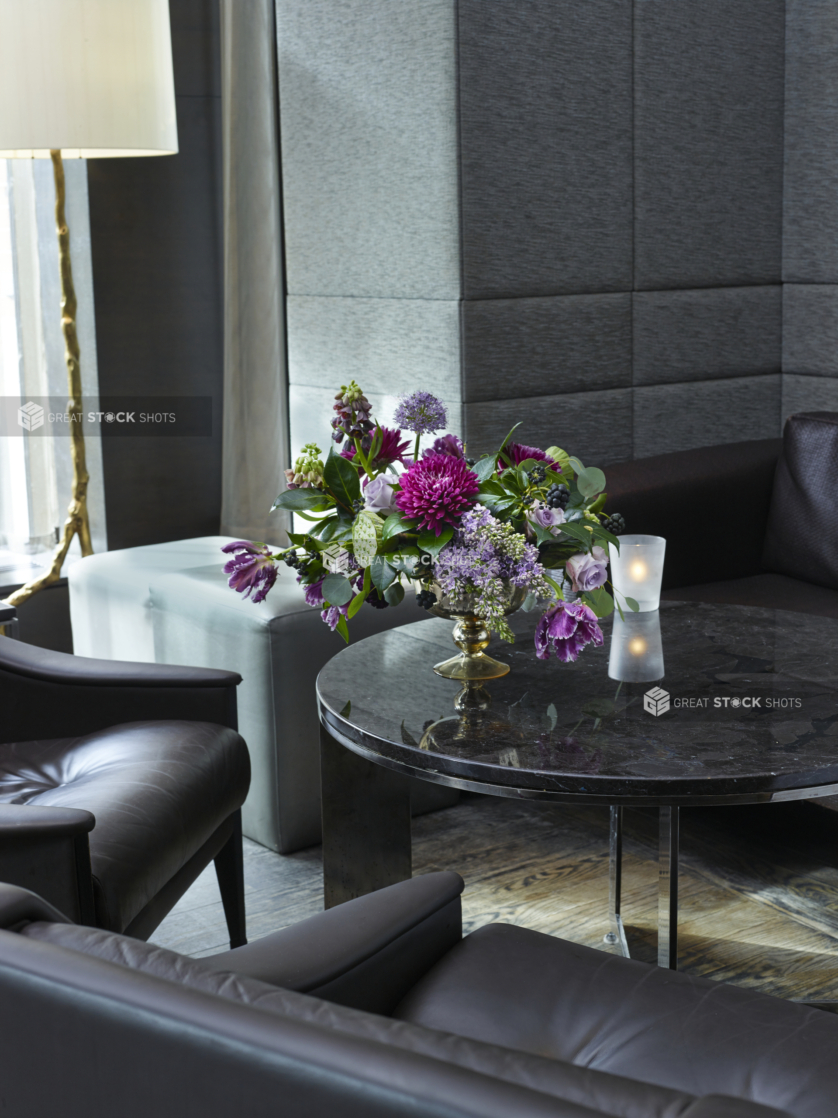 A Large Floral Centrepiece with Purple Dhalias, Parrot Tulips, Fritillaria Persica, Roses, Allium and Lilacs on a Round Glass Coffee Table in an Indoor Setting