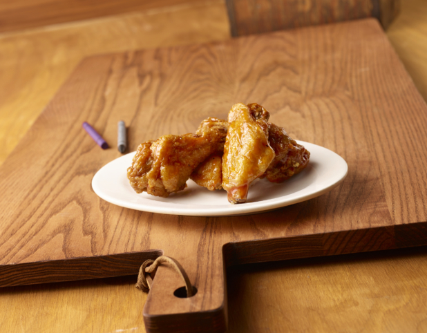 Round White Ceramic Dish of Kid-Sized BBQ Chicken Wings on a Wooden Cutting Board in an Indoor Setting