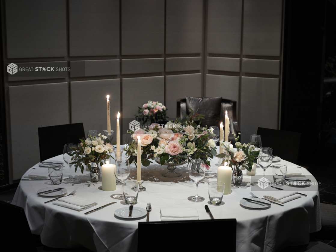 Wedding Reception Table Setting with Pink, White and Peach Rose Floral Arrangements, Candles and Formal Dinnerware on a White Table Cloth