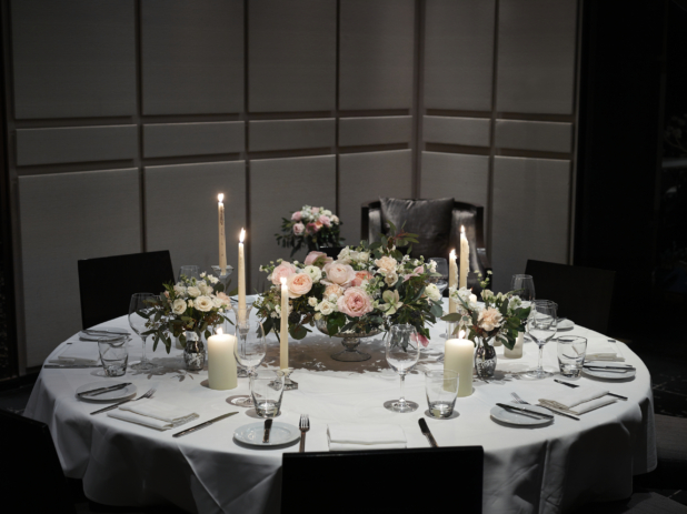 Wedding Reception Table Setting with Pink, White and Peach Rose Floral Arrangements, Candles and Formal Dinnerware on a White Table Cloth