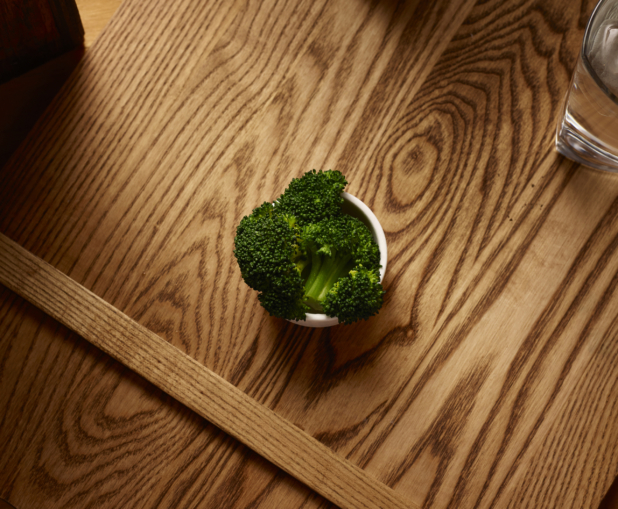 Overhead View of a Small White Ceramic Dish of Kid-Sized Steamed Broccoli Side Dish on a Wooden Cutting Board in an Indoor Setting
