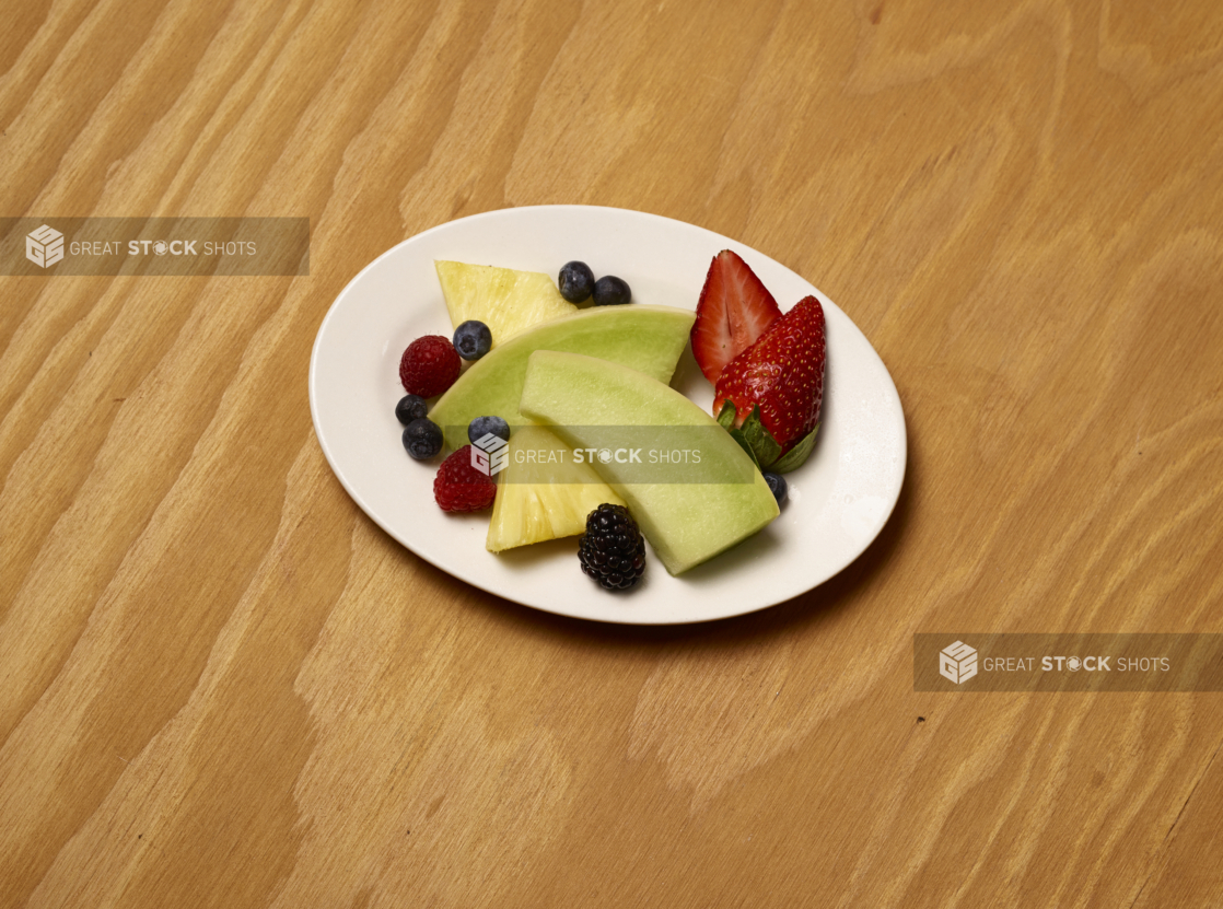 Overhead View of Assorted Cut Fruits and Berries on an White Oval Plate on a Wooden Surface