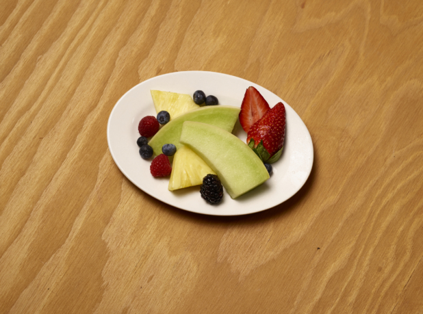 Overhead View of Assorted Cut Fruits and Berries on an White Oval Plate on a Wooden Surface