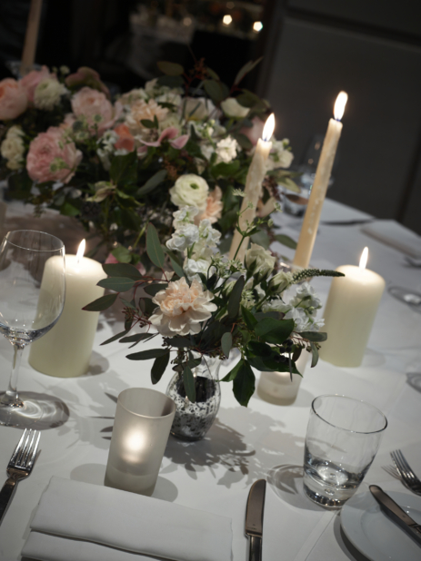 Flower Arrangements and Floral Centrepiece in a Formal Wedding Dinner Setting with White Table Cloth, Folded Napkins and Dinnerware