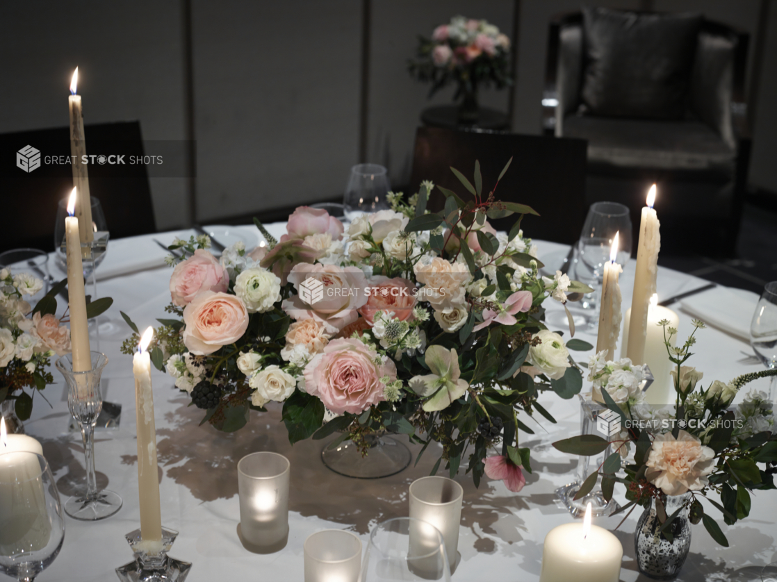 Close Up of a Wedding Reception Table Centrepiece with Pink, White and Peach Rose Floral Arrangements, Candles and Formal Dinnerware on a White Table Cloth