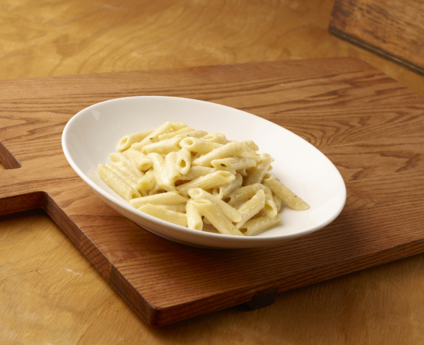 Kids Penne Alfredo Pasta in a Large White Ceramic Bowl on a Wooden Cutting Board in an Indoor Setting