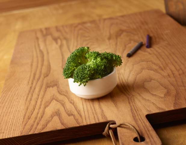 Small White Ceramic Dish of Kid-Sized Steamed Broccoli Side Dish on a Wooden Cutting Board in an Indoor Setting