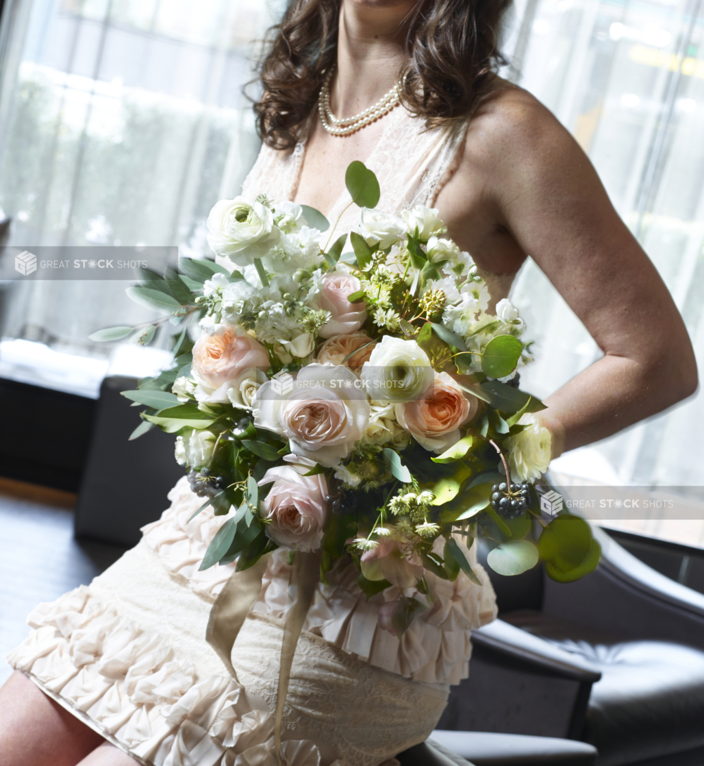 Bride or Bridesmaid in Sleeveless Dress Holding a Large Bouquet of White, Pink and Peach Roses in an Indoor Setting