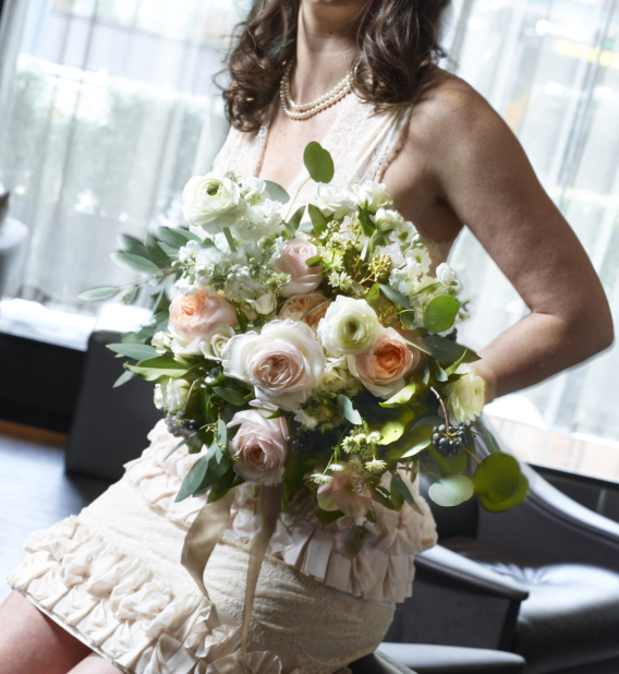 Bride or Bridesmaid in Sleeveless Dress Holding a Large Bouquet of White, Pink and Peach Roses in an Indoor Setting