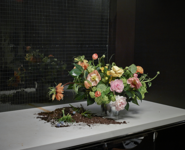 Floral Centrepiece of Light Pink Peonies, Mini White Hydrangeas, Orange Fritillaria and Lotus Seed Pods in Preparation Stages with Pot Soil on a Table