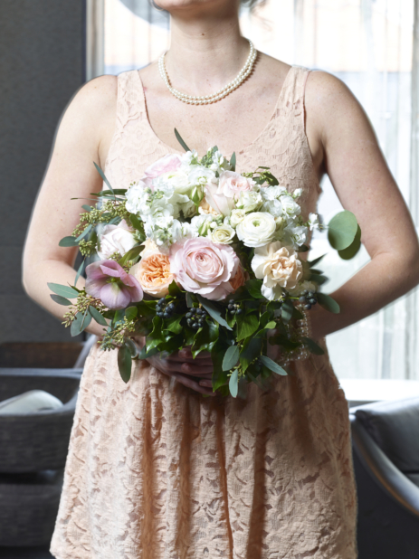 Bridesmaid in Peach Coloured Dress and Wearing Pearl Jewelry Holding a Beautiful Flower Bouquet in an Indoor Setting