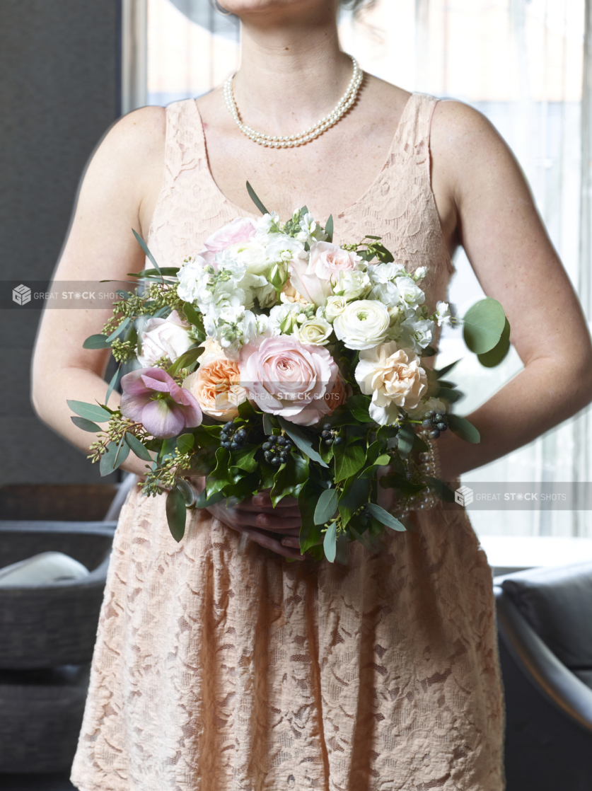 Bridesmaid in Peach Coloured Dress and Wearing Pearl Jewelry Holding a Beautiful Flower Bouquet in an Indoor Setting