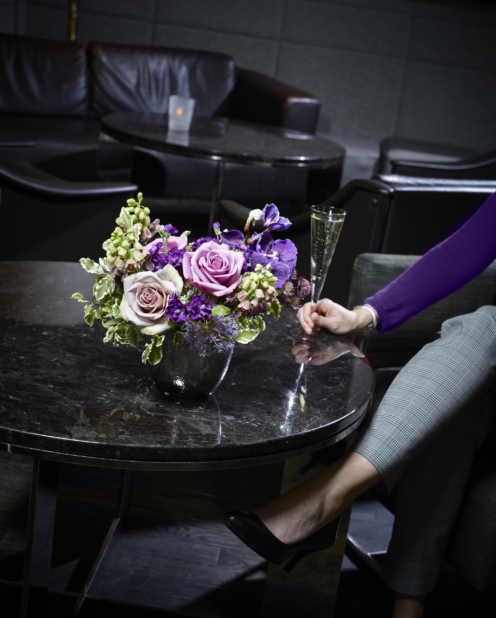 Woman relaxing with a glass of champagne at a low black marble lounge table with a pink and purple rose and iris flower arrangement in a vase