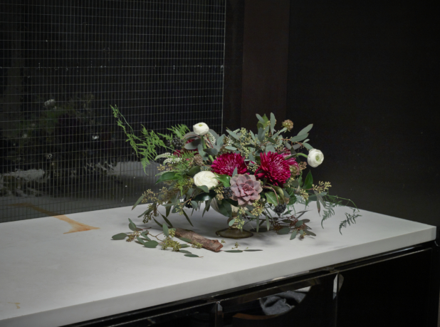 Flower arrangement of red chrysanthemums and white ranunculus on a white marble countertop in front of a mirrored mosaic