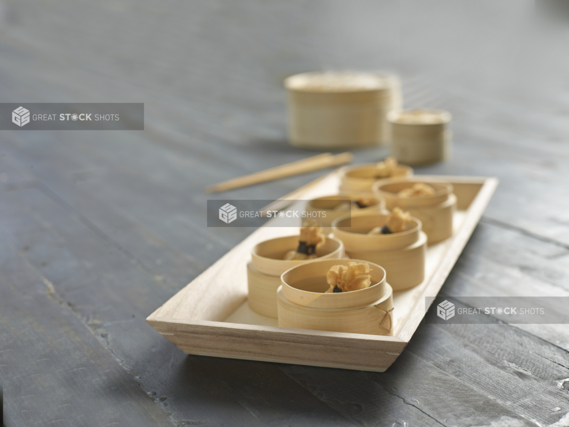 Deep Fried Shrimp Dumpling Bundle Dim Sum in Bamboo Steamer Baskets on a Rectangular Wood Serving Platter in an Indoor Setting