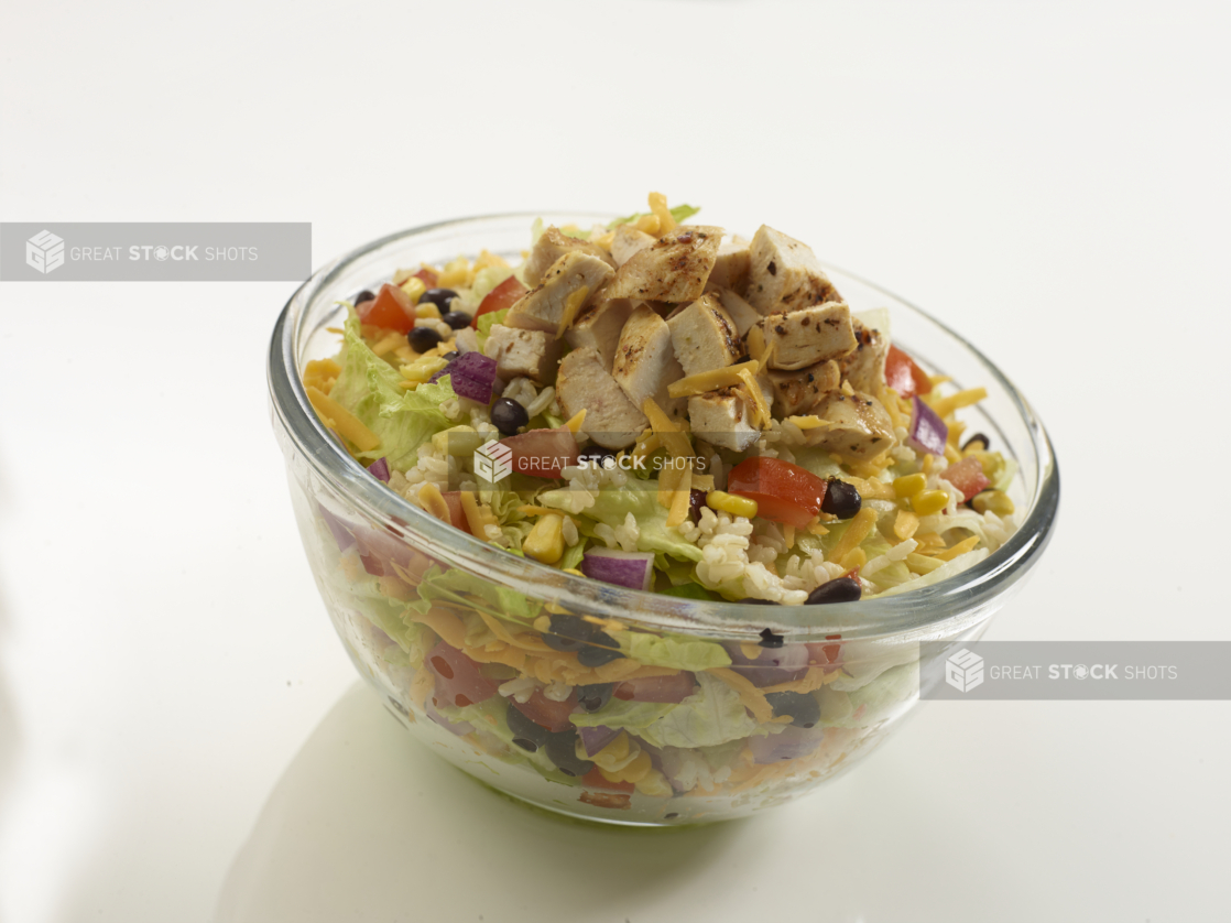 Southwestern-style chopped salad with grilled chicken in a clear glass bowl on a reflective white surface