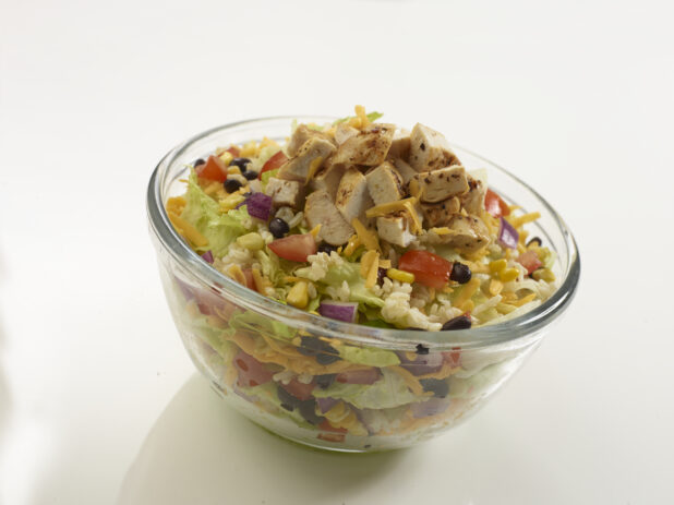 Southwestern-style chopped salad with grilled chicken in a clear glass bowl on a reflective white surface