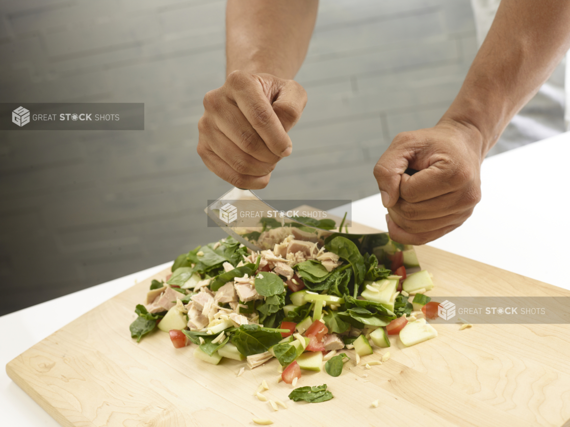 Chef using a mezzaluna knife to chop salad ingredients