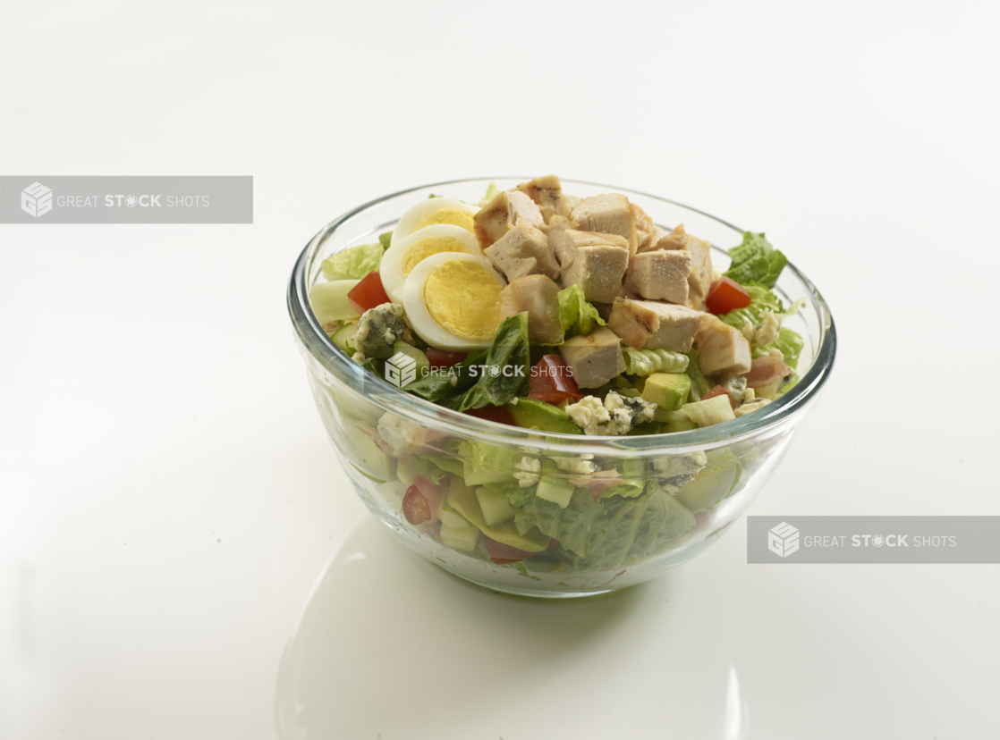 Grilled chicken Cobb salad in a clear glass bowl on a reflective white surface