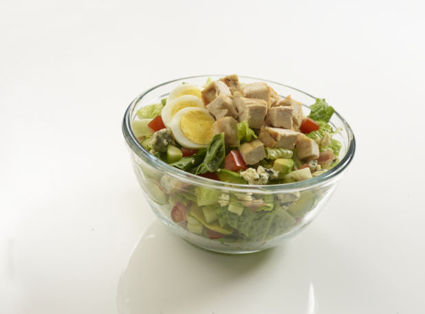 Grilled chicken Cobb salad in a clear glass bowl on a reflective white surface