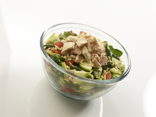 Spinach salad with tuna, cucumbers, tomato, and slivered almonds in a clear glass bowl on a reflective white surface