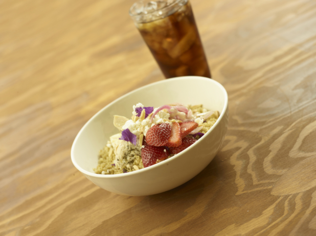 A Breakfast Bowl of Quinoa, Sliced Strawberries, Sliced Almonds and Yogurt with a Glass of Diet Coke and Ice on a Wooden Table in an Indoor Setting