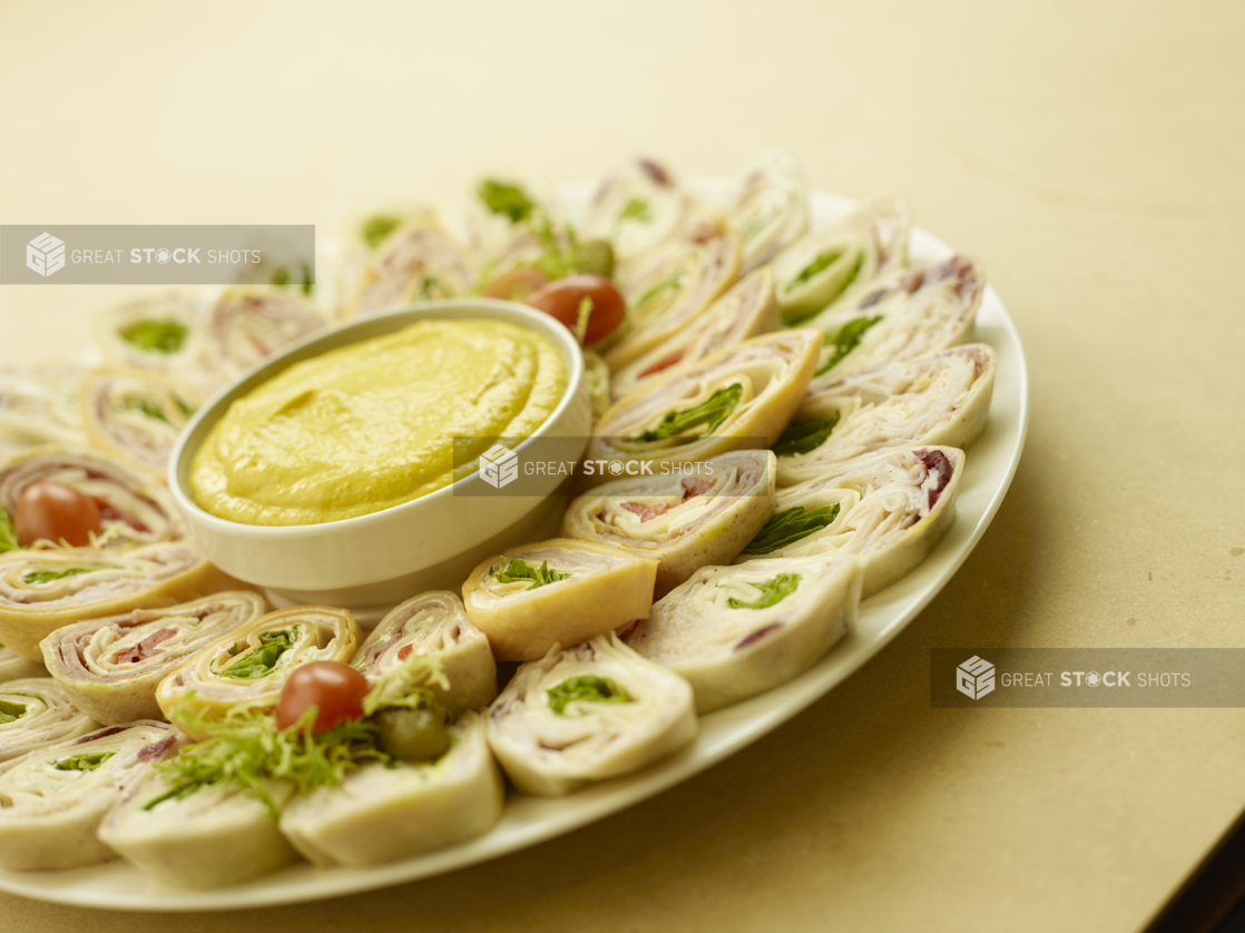 A Platter of Mini Turkey and Ham Wrap Sandwiches with a Yellow Dipping Sauce for Catering