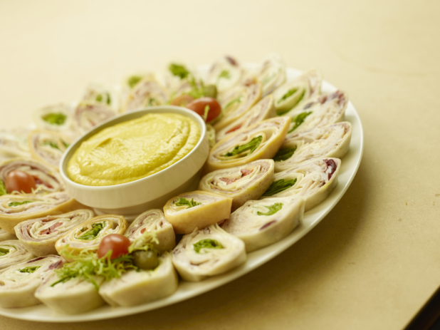 A Platter of Mini Turkey and Ham Wrap Sandwiches with a Yellow Dipping Sauce for Catering