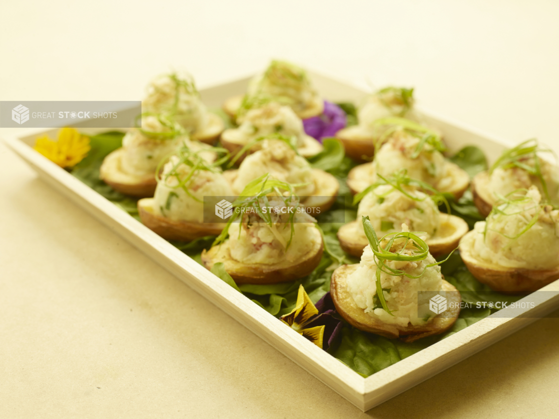 A Rectangular Wooden Serving Tray with Stuffed Potato Skins with Bacon and Chives and Spring Onion Garnish on a Bed of Lettuce for Catering