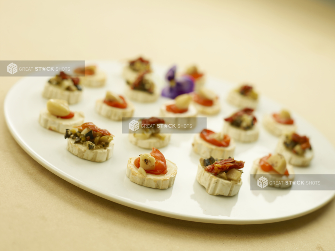 A Large Round White Platter Dish of Hors D'Oeuvres of Roasted Red Pepper, Sun-dried Tomatoes, Roasted Garlic on a Mini Brie Slice for Catering