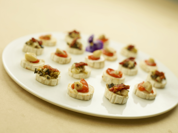 A Large Round White Platter Dish of Hors D'Oeuvres of Roasted Red Pepper, Sun-dried Tomatoes, Roasted Garlic on a Mini Brie Slice for Catering