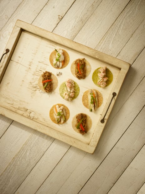 Overhead View of a Painted Wooden Tray of Assorted Soft Tacos (Grilled Chicken, Lobster Salad, Korean Bulgogi Beef) for Catering on a Panelled Wooden Surface in an Indoor Setting