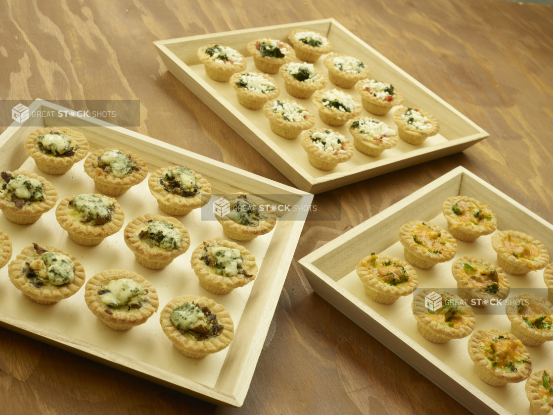 Shallow Wood Serving Trays of Assorted Mini Quiches (Spinach and Mushroom, Cheddar and Broccoli, Quiche Lorraine) for Catering on a Wooden Table