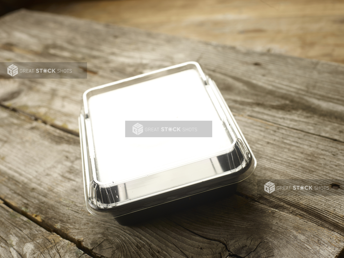 Rectangular Plastic Take-Out Container with Clear Lid and Black Base on Aged Wooden Table - Closed Lid