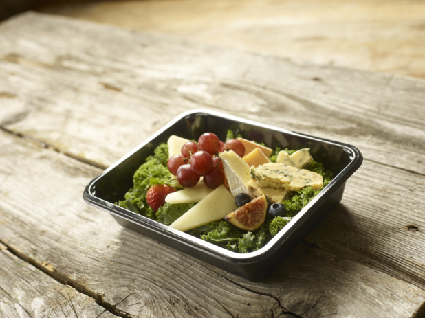 A Healthy Snack of Assorted Cheese Slices, Fruits on a Bed of Lettuce in a Black Take-Out Container on a Wooden Table