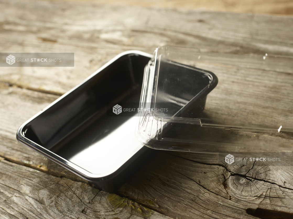 Rectangular Plastic Take-Out Container with Clear Lid and Black Base on Aged Wooden Table – Open Lid; Variation